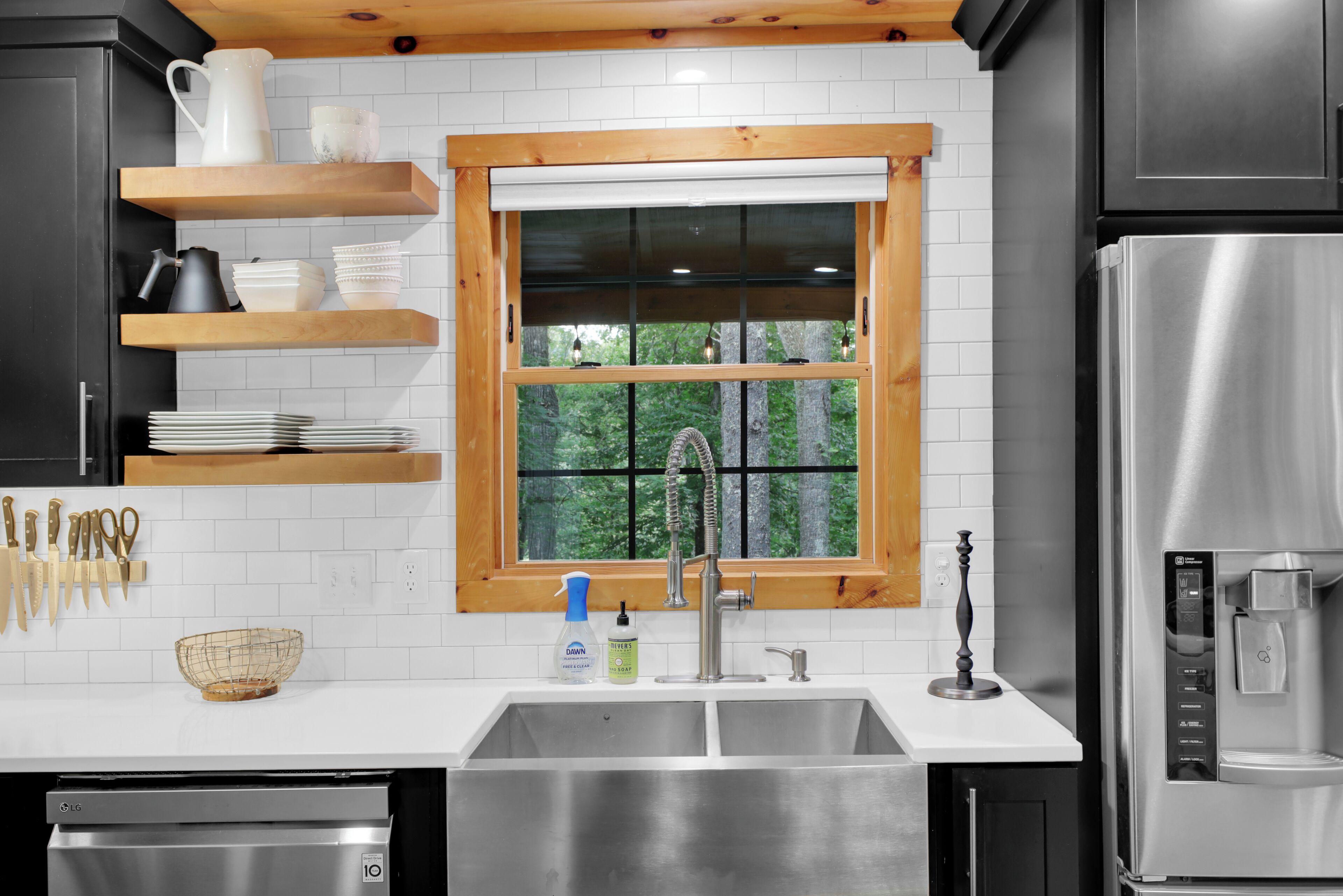 A modern kitchen with a stainless steel refrigerator, double sink, and wooden shelves.