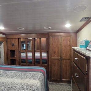 Ein Schlafzimmer mit Bett, Holzschrank und einem Badezimmer mit Spiegel und Handtuchspender.