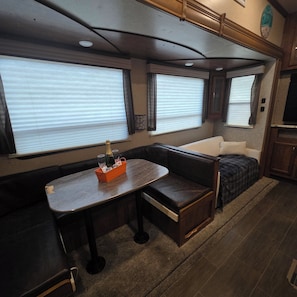 A compact RV interior with a dining area, a seating bench, and a small bed.