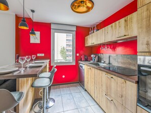 A modern kitchen with red walls, wooden cabinets, and a dining area with bar stools. - Appartement Ollier - Welkeys (Villeurbanne)