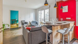 Une cuisine moderne avec un mur d’accent rouge, un coin bar et un espace détente avec un canapé et des fauteuils.