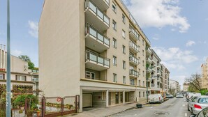 Un immeuble résidentiel à plusieurs étages, doté de balcons, d’une entrée sécurisée et d’un espace de stationnement avec des voitures.