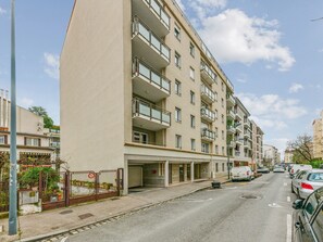 A multi-story residential building with balconies, a gated entrance, and a parking area with cars. - Appartement Ollier - Welkeys (Villeurbanne)