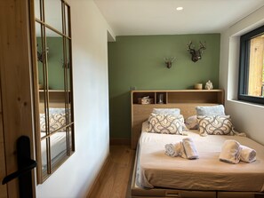 A bedroom with a bed, pillows, a bedside table, a window, and a wall-mounted deer head decoration. - Chalet Vue des Bossons - Welkeys (Chamonix-Mont-Blanc)