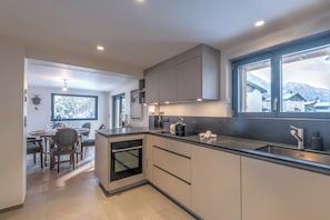 A modern kitchen with a built-in oven, a large window with a view of mountains, and a dining area with a table and chairs. - Chalet Vue des Bossons - Welkeys (Chamonix-Mont-Blanc)