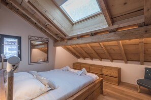 Un dormitorio con tragaluz, vigas de madera, una cama con ropa de cama blanca, una mesita de noche y una silla.