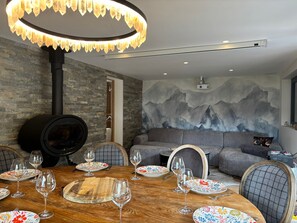 A modern dining area with a wooden table set for six, surrounded by grey sofas and a stone wall. - Chalet Vue des Bossons - Welkeys (Chamonix-Mont-Blanc)