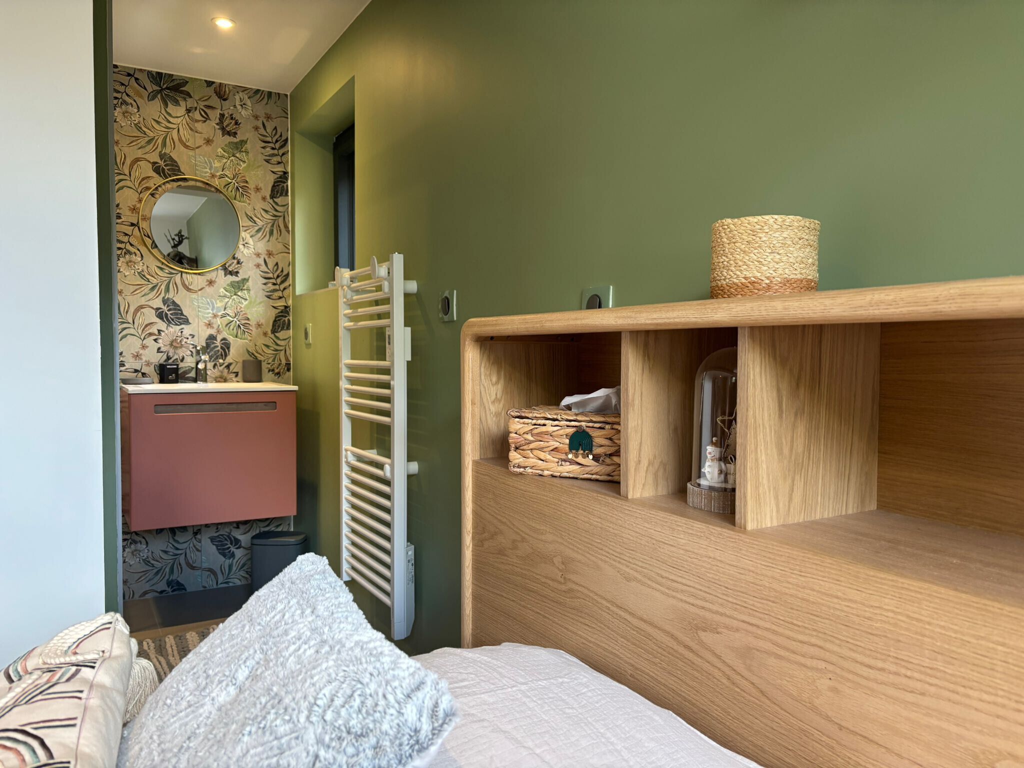 Een slaapkamer met een bed, een houten dressoir, een spiegel, een handdoekhouder en een wand met bloemenbehang.