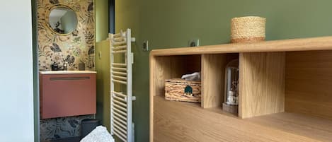 Een slaapkamer met een bed, een houten dressoir, een spiegel, een handdoekhouder en een wand met bloemenbehang.