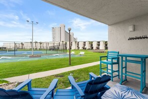 Ett poolområde med blå Adirondack-stolar, en tennisbana och en byggnad i bakgrunden med skylten ”Susan Beach C33”.