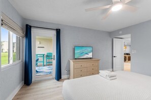 Ein Schlafzimmer mit Bett, Fernseher auf einer Kommode, Deckenventilator und Blick ins Freie.