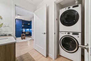 A laundry room with two stacked washing machines, a small table with a chair, and a desk with a computer.