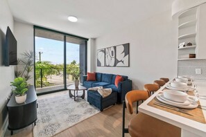 A modern living room with a sofa, coffee table, and a dining area with chairs and a table set for a meal.