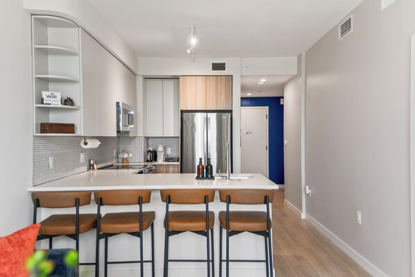 Une cuisine moderne avec un îlot central, des tabourets de bar et un mur d’accent bleu.