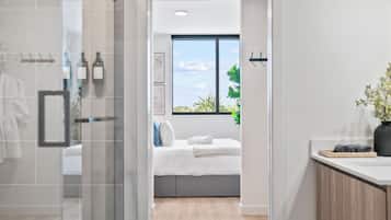 Een moderne badkamer met een glazen douchecabine, een zichtbare handdoekhouder en een groot raam met uitzicht op groen.