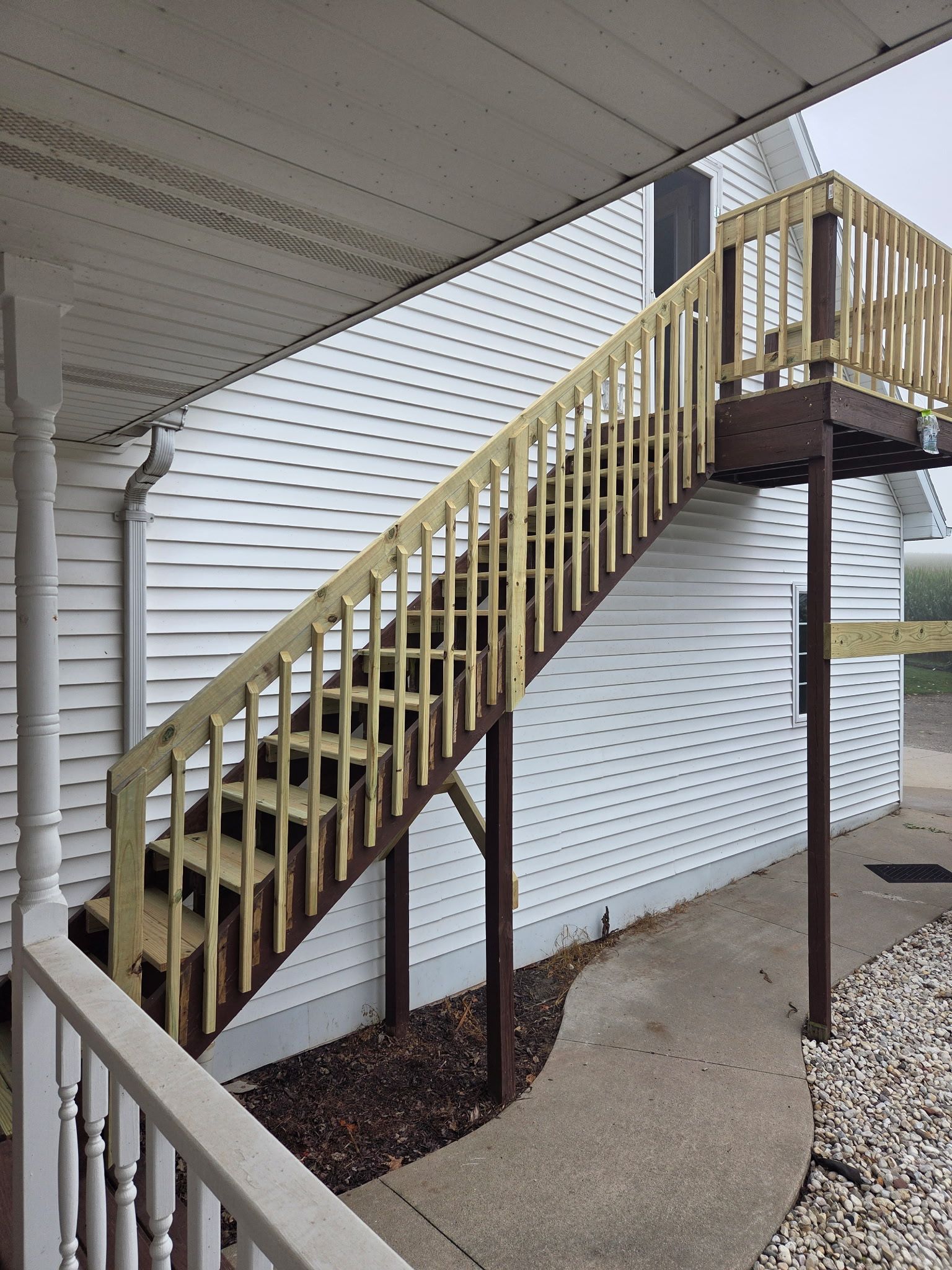 A wooden staircase leading to a covered porch area with a white exterior wall.