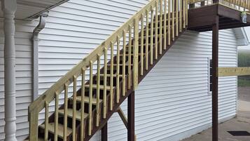 A wooden staircase leading to a covered porch area with a white exterior wall.