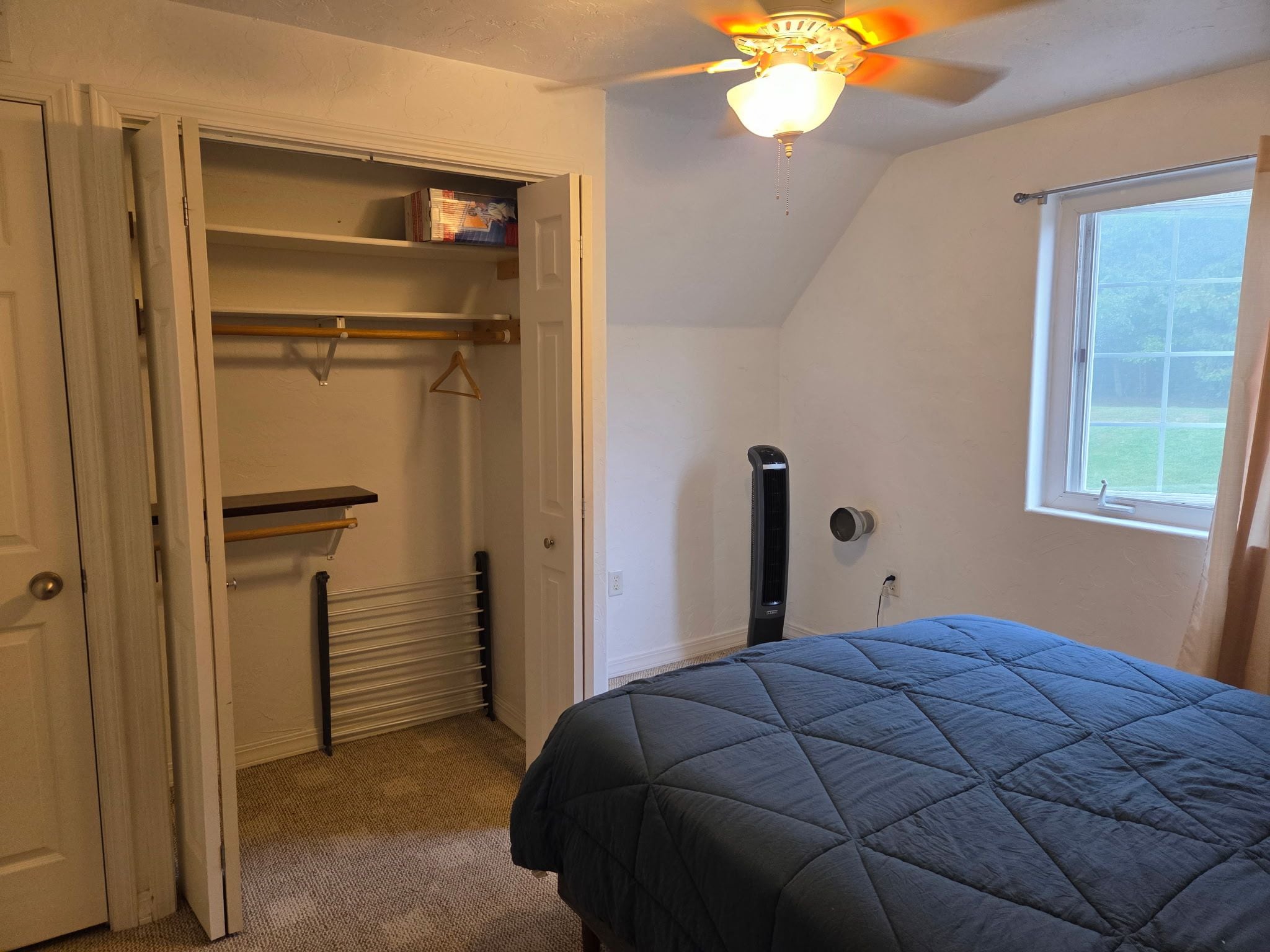 A bedroom with a bed, a closet with shelves, a radiator, and a window.