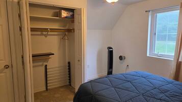 A bedroom with a bed, a closet with shelves, a radiator, and a window.