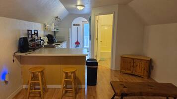 A compact kitchen with a bar area, wooden stools, a trash bin, and a wooden bench.