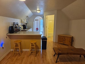 Een kleine keuken met een bar, houten krukken, een prullenbak en een houten bank.