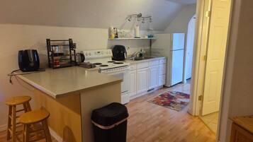 A kitchen with a central island, wooden stools, a trash bin, and a refrigerator.