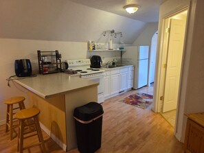 Een keuken met een centraal eiland, houten krukken, een afvalbak en een koelkast.