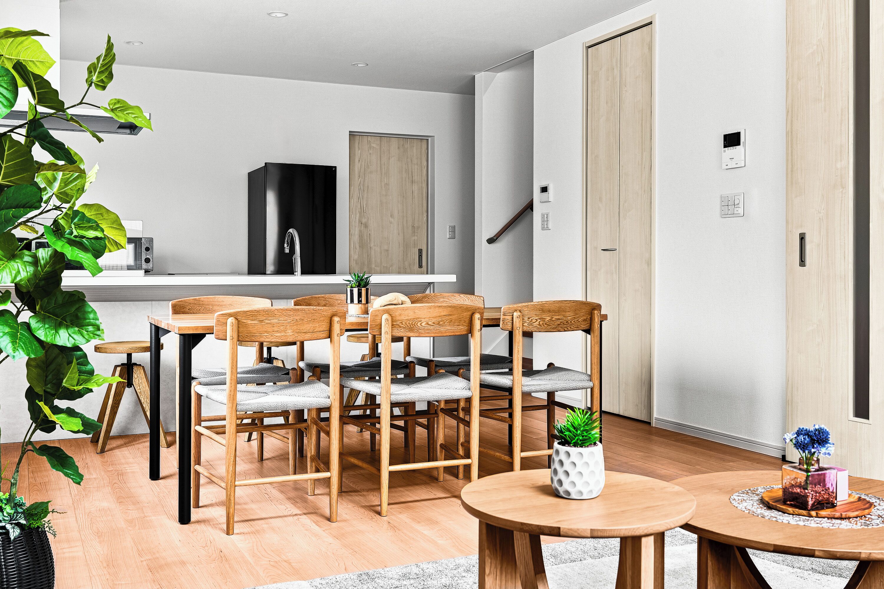 A modern kitchen with a dining area, wooden furniture, and potted plants.