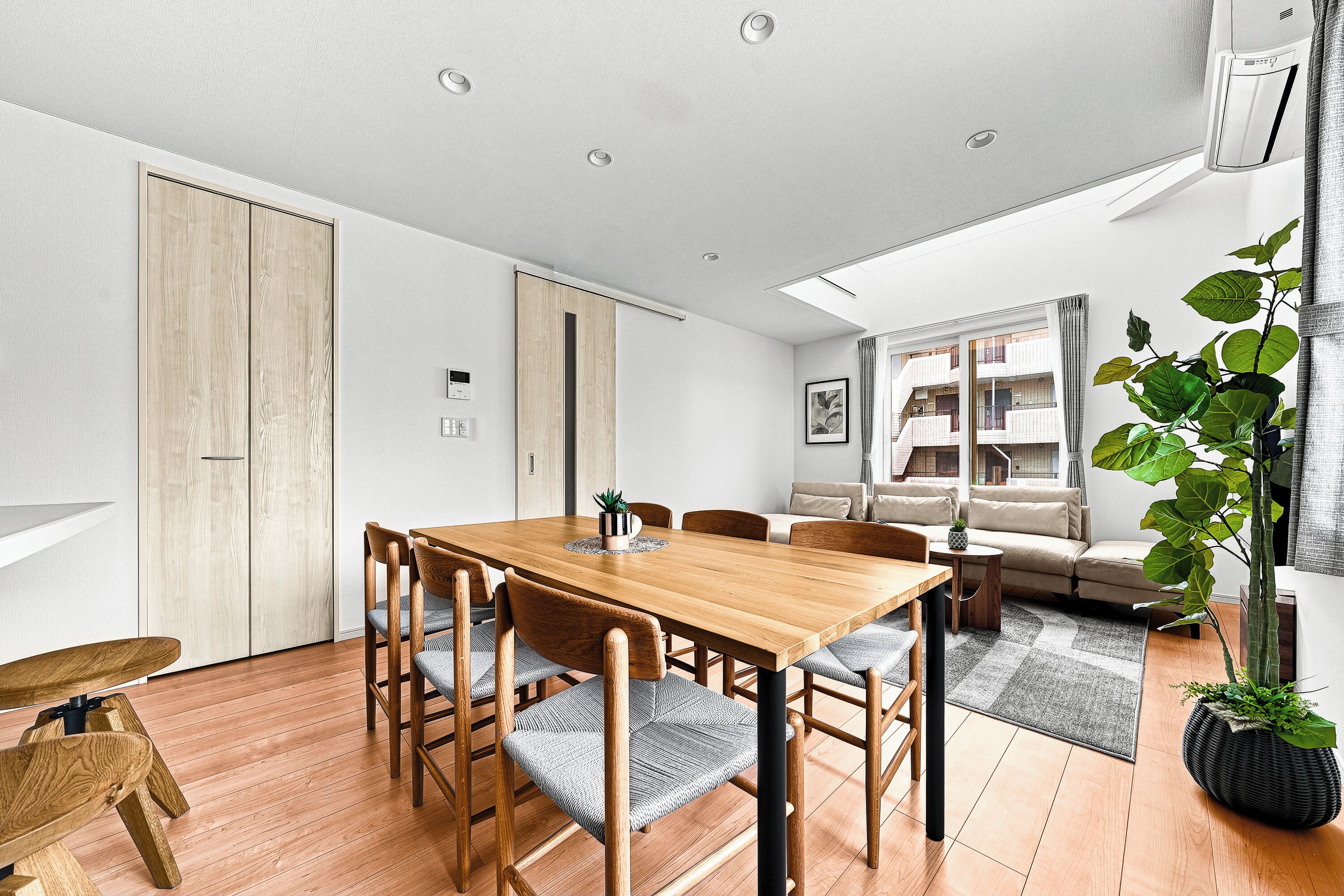 A modern interior with a wooden dining table, chairs, a sofa, and a large plant.