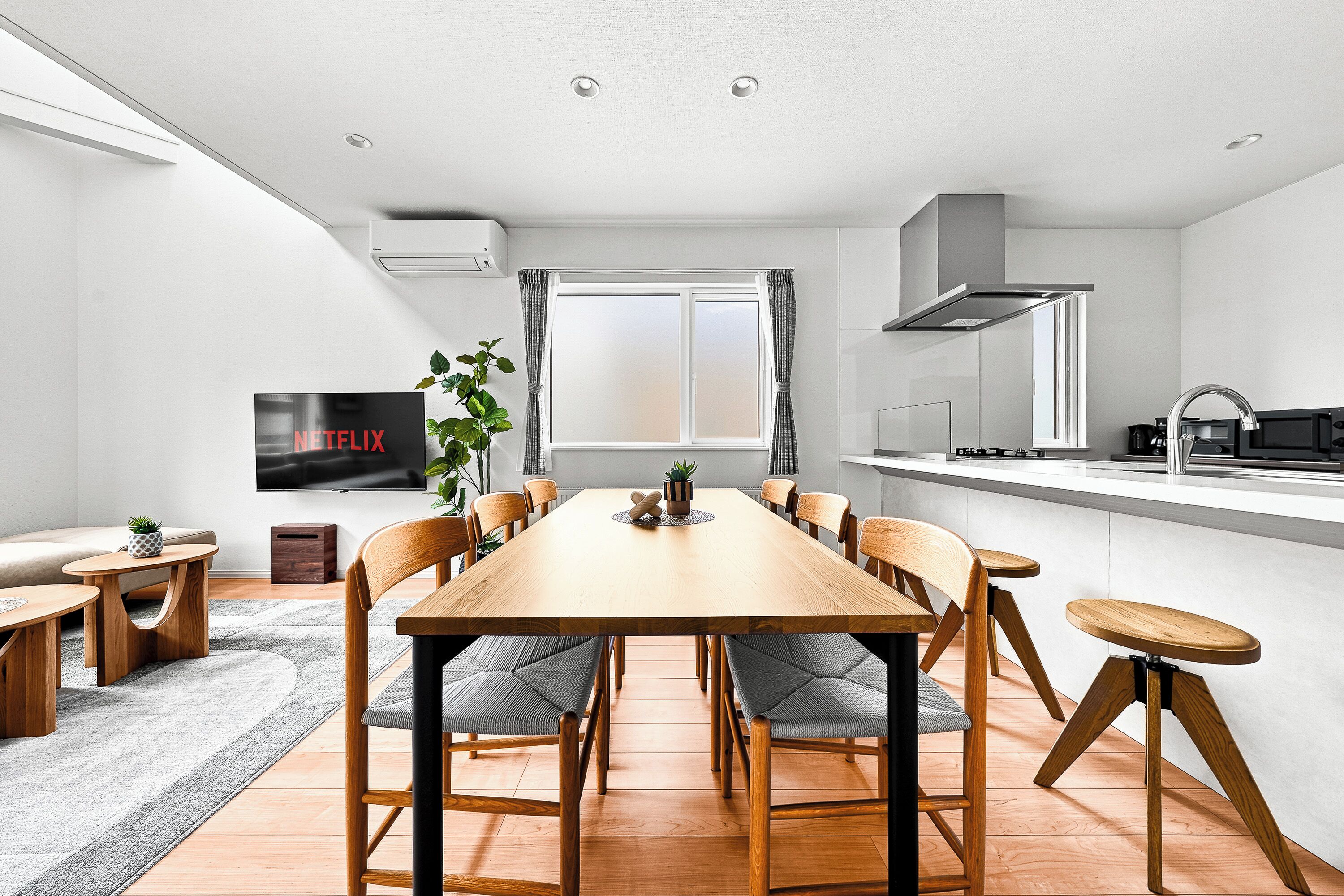 A modern kitchen with a dining area, a TV, and a window with curtains.