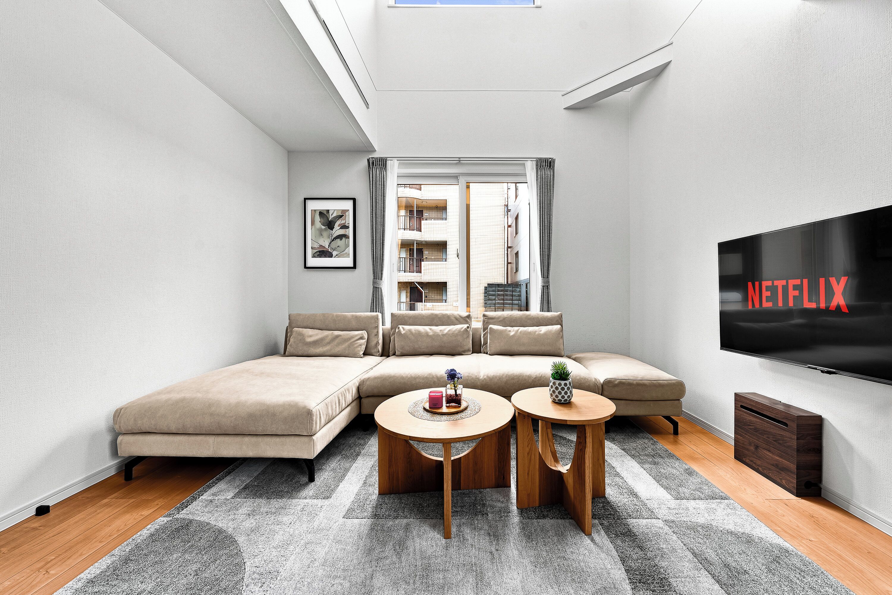 A modern living room with a sectional sofa, a flat-screen TV, and a view of a building through a window.
