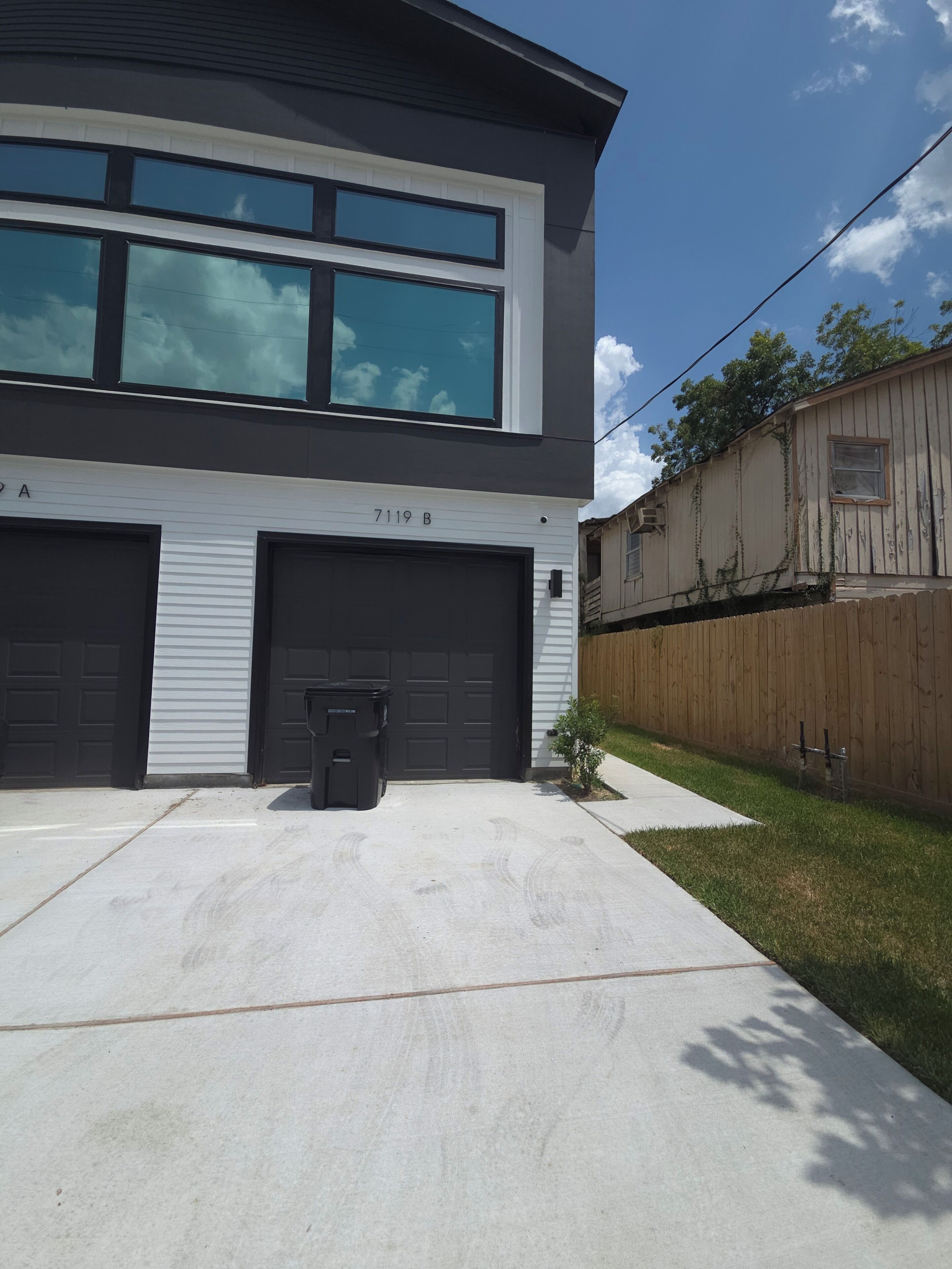 Una casa moderna de dos pisos con garaje, un pequeño patio delantero y una cerca de madera.