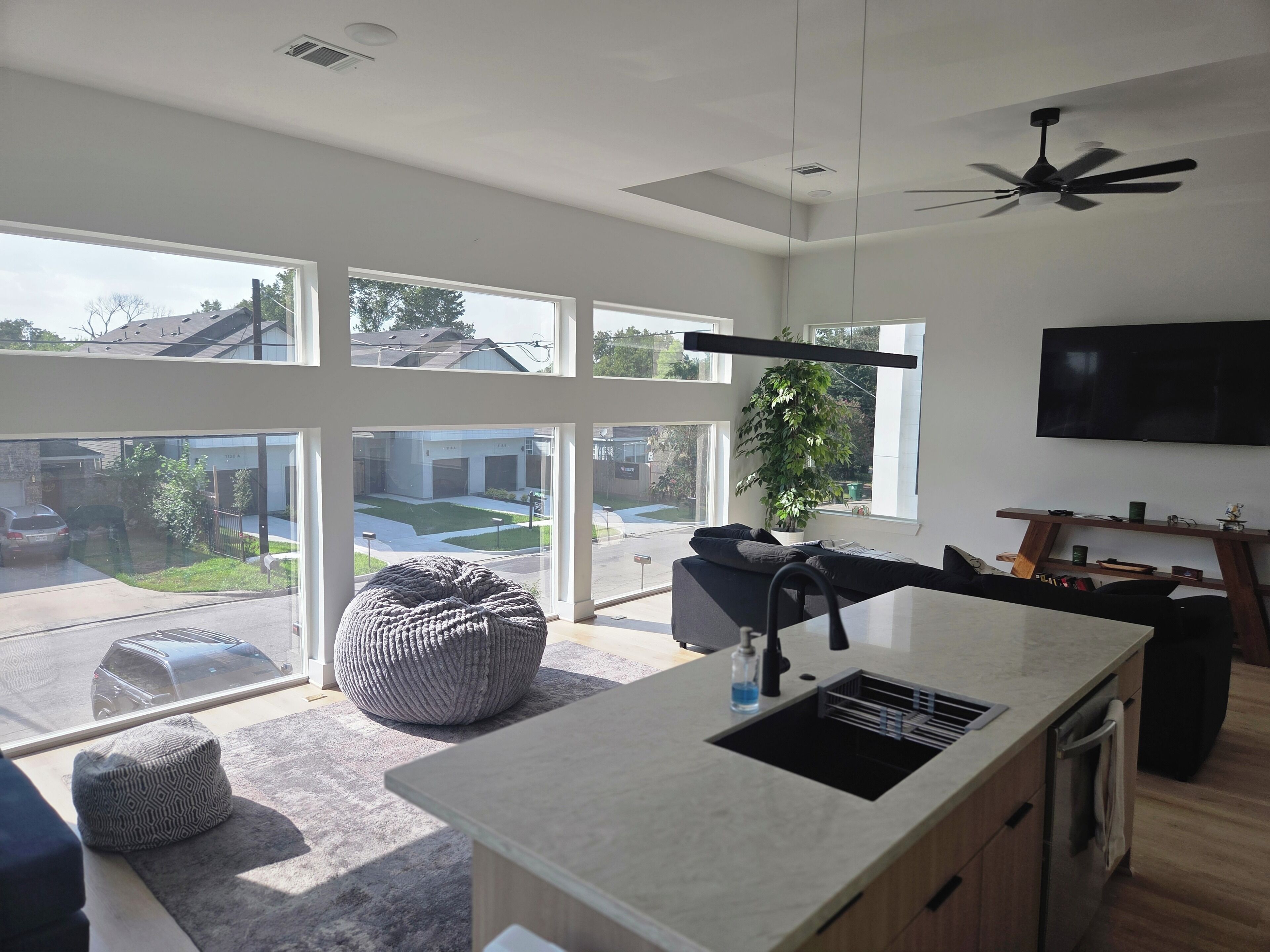 A modern kitchen with large windows, a ceiling fan, and a flat-screen TV.