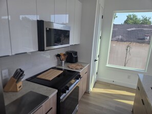 A modern kitchen with white cabinets, a microwave, a stove, and a window overlooking a backyard. - NEW! Houston Retreat, Near Medical District, NRG Stadium & Downtown (Houston)