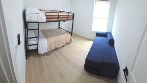 Ein Zimmer mit Etagenbett, Einzelbett und einem Fenster mit Jalousien.