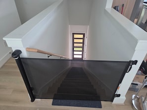 A staircase with a black safety gate, a wooden handrail, and a black mat at the bottom. - NEW! Houston Retreat, Near Medical District, NRG Stadium & Downtown (Houston)