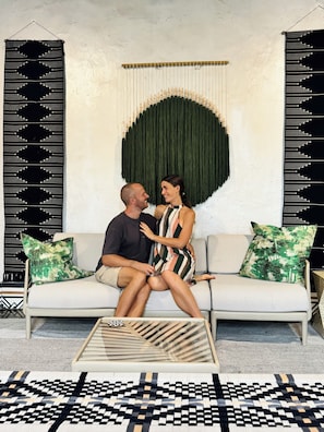 A couple sitting on a sofa with a patterned rug, a green wall art piece, and a patterned wall. - Historic Colonial Designer Home (Granada)