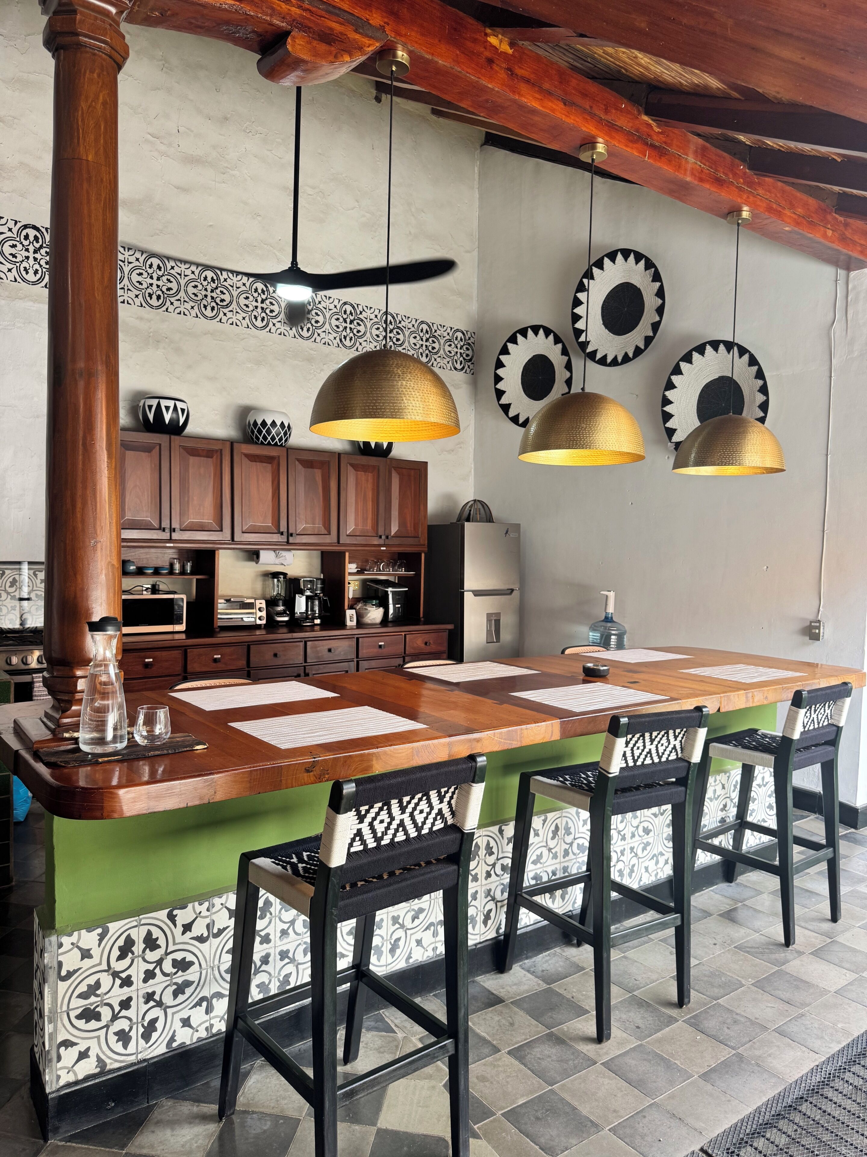 A kitchen with a wooden island, hanging pendant lights, and patterned wall decor.