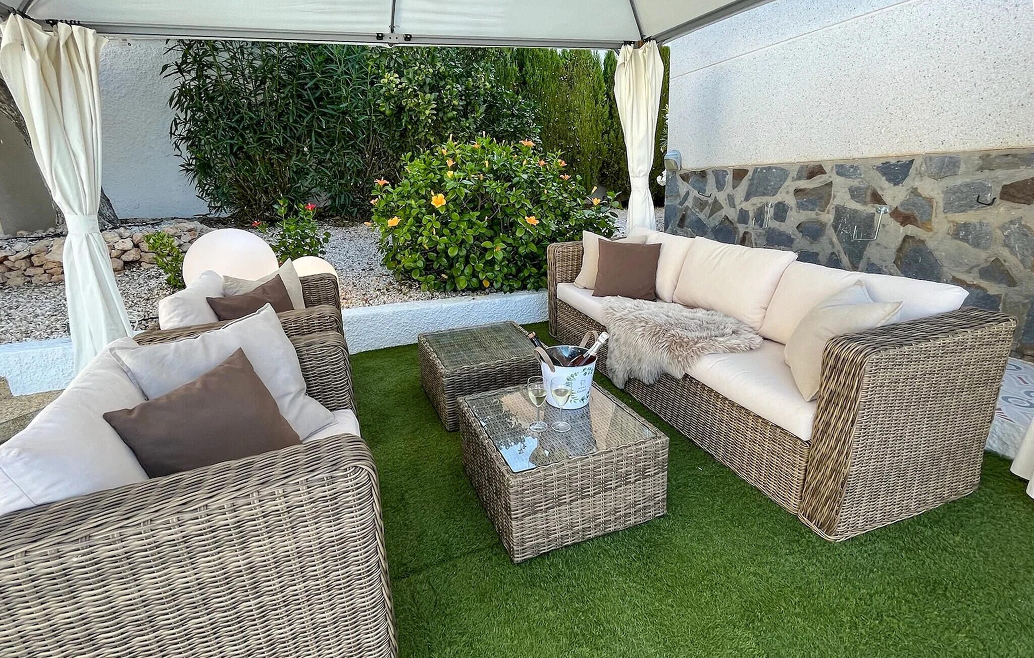 An outdoor seating area with wicker furniture, a glass table, and a stone wall backdrop.
