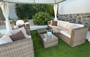 An outdoor seating area with wicker furniture, a glass table, and a stone wall backdrop. - Lovely home in Rojales with sauna (Rojales)
