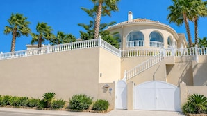 Un edificio de dos plantas con fachada color beige, balcones blancos y palmeras.