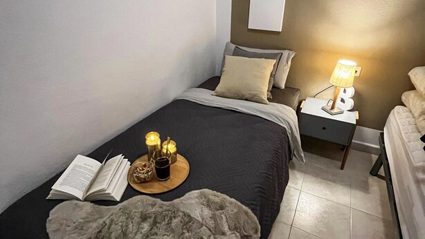 A bedroom with a bed, bedside table, lamp, and a book on the bed.