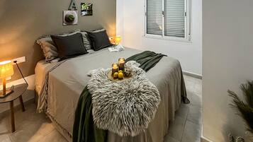 A bedroom with a bed, pillows, a bedside table with a lamp, a window with blinds, and wall decorations.