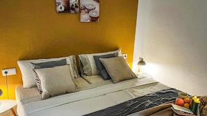 Una cama con una colcha blanca y gris, dos almohadas y una mesita de noche con una lámpara.