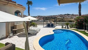 A swimming pool with a curved edge, surrounded by a patio with lounge chairs and a pergola.