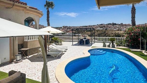 Una piscina con borde curvo, rodeada por un patio con sillones de descanso y una pérgola.
