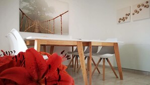 Un comedor con mesa de madera y sillas blancas, un cuadro de un puente y una pared con adornos circulares.