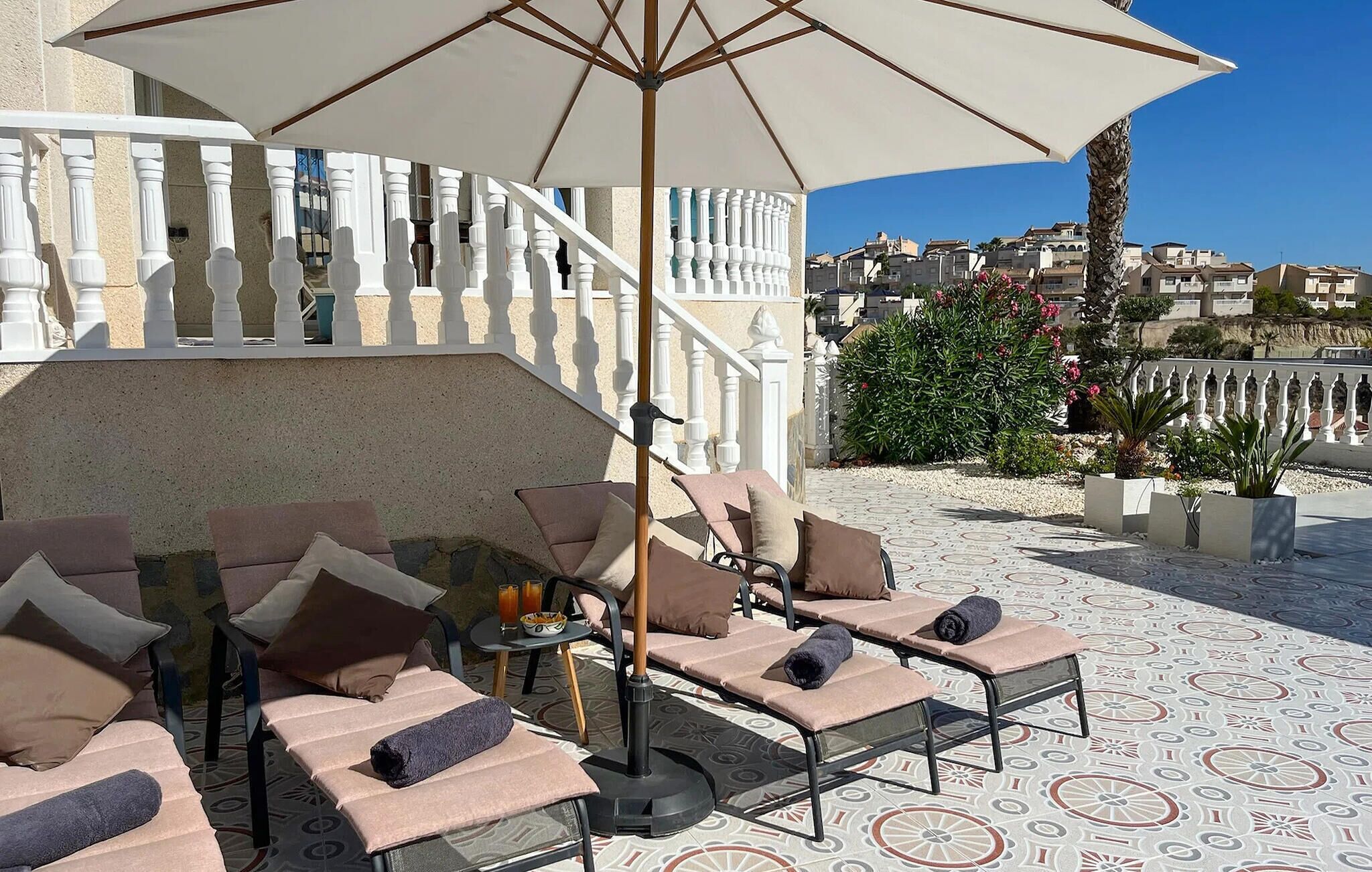Una terraza con sillones de descanso, una mesa con bebidas y un gran paraguas.