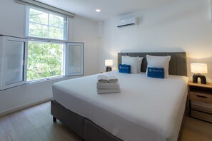 A hotel room with a large bed, two bedside tables, a window with a view of trees, and an air conditioning unit on the wall. - History, Comfort & Character in Willemstad (Willemstad)