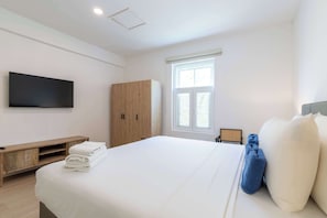 Ein Hotelzimmer mit Bett, Wandfernseher, Kleiderschrank und Fenster mit Jalousien.
